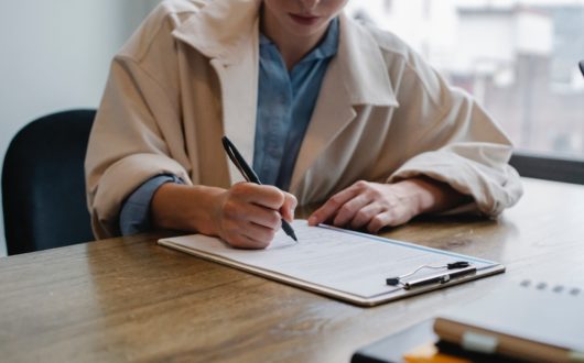 Women in a khaki jacket sits at a table filling out an application on a clipboard