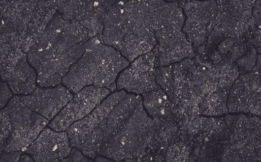 Close-up of road asphalt with spidering cracks through the surface